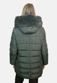 Cappotto imbottito verde scuro con cappuccio in pelliccia sintetica. Presenta una texture trapuntata, motivi lucidi e maniche lunghe. La vista posteriore mostra il cappuccio e i polsini.
