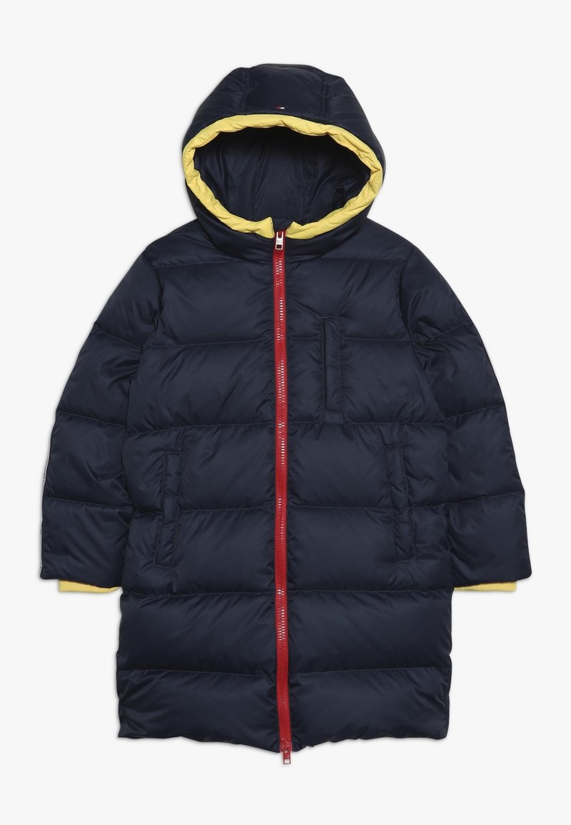 Námořnický modrý prošívaný kabát s žlutou podšívkou kapuce a červeným zipem. Obsahuje boční kapsy a prošívanou strukturu pro izolaci.