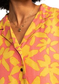 Short-sleeve shirt with a pink and yellow floral pattern, made of lightweight fabric; features a collar and a front button closure.