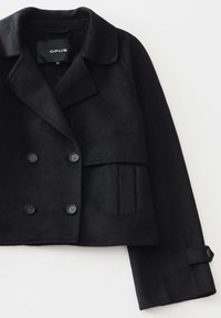 Giacca cropped in misto lana nera con chiusura doppiopetto, colletto a rever e due tasche frontali. Bottoni neri e linee pulite.