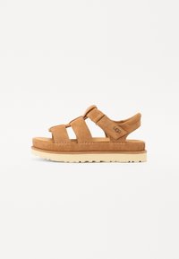Brune suedine sandaler med tre brede stropper, polstret mellomsåle og en slitesterk gummisåle i lys farge. Har UGG-merket på siden.