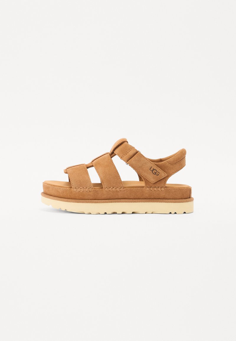 Brune suedine sandaler med tre brede stropper, polstret mellomsåle og en slitesterk gummisåle i lys farge. Har UGG-merket på siden.