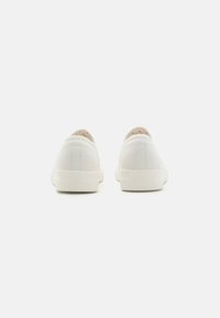 Witte canvas sneakers met een laag profiel, platte crème rubberen zool en zichtbare stiksels op de hiel en zijkanten.