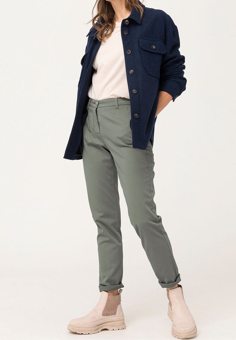 Námořnická košile z vlněné směsi s knoflíkovým zapínáním, světle béžové bavlněné tričko, zelené tapered kalhoty a světle béžové kotníkové boty s elastickými akcenty.