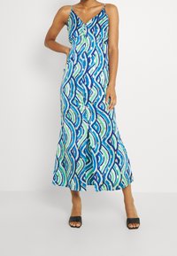 Robe longue à motif ondulé bleu, vert et blanc avec bretelles fines, col en V et détails de boutons à l'avant. Texture de tissu lisse.