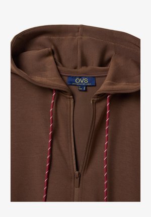 Sudadera con capucha marrón con cremallera, cordones rojos y blancos, y una etiqueta azul en el interior del cuello que dice "OVS" y muestra la información de talla.