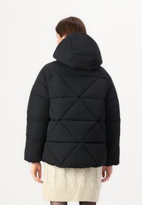 Zwarte gewatteerde jas met een capuchon, met een diamanten quiltpatroon. De stof is soepel en de mouwen zijn iets oversized.