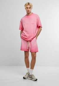 Tricou roz tie-dye și șorturi asortate dintr-un material moale. Tricoul are o croială lejeră, cu guler rotund; șorturile au un talie elastică și șnur de ajustare.