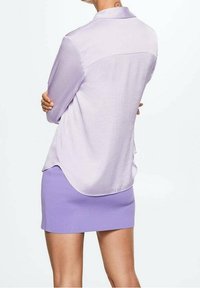 Chemise à manches longues violet clair avec un ourlet arrondi, en tissu lisse. Associée à une mini-jupe moulante violet clair.