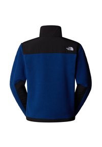 Niebieska bluza polarowa z czarną górną częścią i kołnierzem. Posiada teksturowane wykończenie oraz logo na plecach. Długie rękawy i prosty dół.