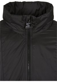Black puffer jacket with a high collar, featuring a central zipper and a silver logo accent. Textured, lightweight fabric.