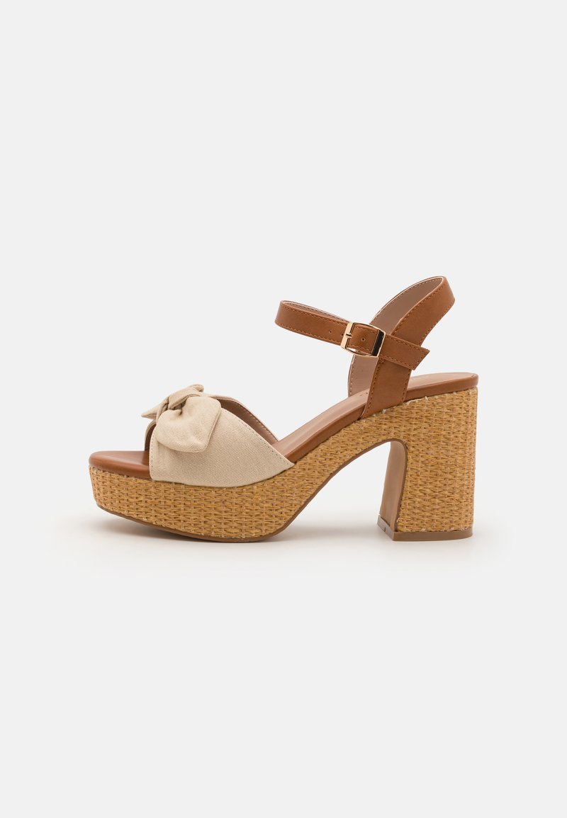 Beige fabric upper with a front bow detail, brown ankle strap, and woven platform heel. Features a chunky block heel design.