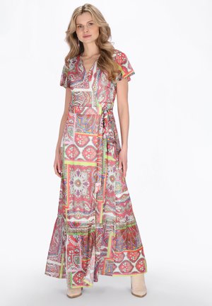 Donna che indossa un vestito lungo a portafoglio con motivi colorati, maniche corte e stivaletti beige con tacco su sfondo bianco.