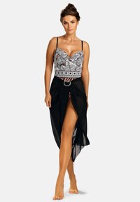 Strój kąpielowy z czarno-białym wzorem liści i koronkowym wykończeniem, w zestawie z przezroczystą czarną sarongą z rozcięciem z przodu i okrągłym metalowym detalem.