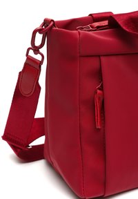 Borsa di stoffa rossa con texture liscia, forma rettangolare, tracolla regolabile e una piccola tasca esterna con zip. Presenta una chiusura superiore sicura.