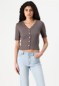 Gray ribbed crop top with short sleeves, scalloped edges, and buttoned front. Paired with light blue denim jeans.