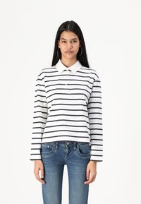 Long-sleeve polo in white with navy horizontal stripes, featuring a classic collar, button front, and relaxed fit, paired with blue jeans.