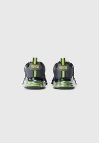 Sapatilhas pretas com detalhes verdes, material em malha e sola transparente. Apresentam uma aba do calcanhar com a marca e riscas contrastantes na parte traseira.