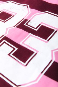 Pogled od blizu na tkanino s roza in maroon vodoravnimi črtami ter velikim belim številom "23" obrobljenim v roza in maroon.