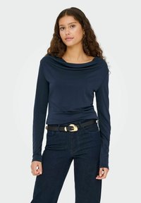 Mørkeblå langærmet top med en bølget halsudskæring. Blødt stof, tætsiddende design, kombineret med mørke jeans og et sort bælte med en guldbuckle.