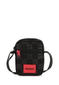 Borsa a tracolla in tessuto nero con motivo ripetuto del logo "HUGO". Presenta una zip rossa e una patch logo rosa di forma rettangolare.