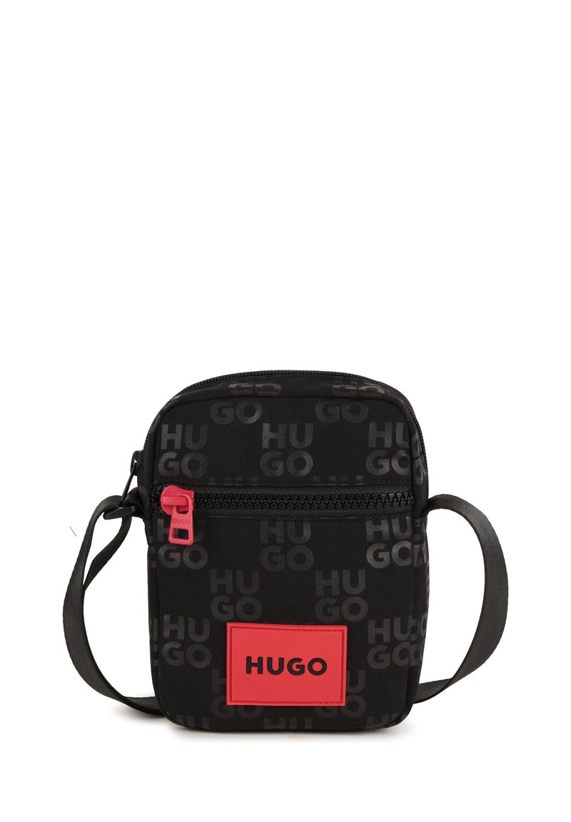 Borsa a tracolla in tessuto nero con motivo ripetuto del logo "HUGO". Presenta una zip rossa e una patch logo rosa di forma rettangolare.