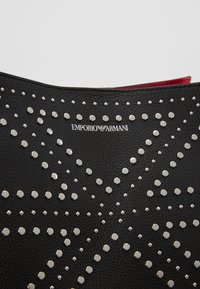 Czarna skórzana torebka z srebrnymi ćwiekami w wzór gwiazdy. Wnętrze wyłożone jest na czerwono; logo nadrukowane blisko góry.