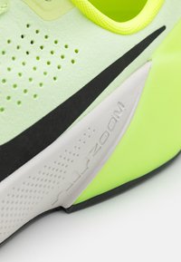 Primo piano di una sneaker Nike verde neon che mostra il logo swoosh nero e una suola intermedia grigia con il testo "air zoom" in rilievo.