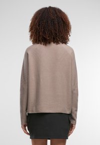 Beežist tekstuuriga kampsun pikkade varrukatega, lõdva lõikega ja lühendatud seljaga, millele on lisatud must seelik küljetaskutega.