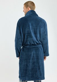 Peignoir de bain en polaire douce bleu marine, avec col châle, ceinture à nouer et manches longues. Présente une surface texturée et un design jusqu'aux genoux.