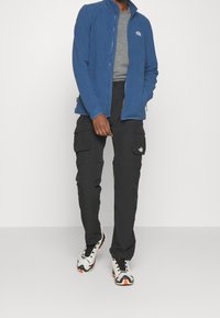 Niebieska kurtka z polaru na zamek, szary t-shirt, czarne spodnie typu cargo oraz wielokolorowe trampki na sznurowadła. Kieszenie w spodniach, logo na kurtce.