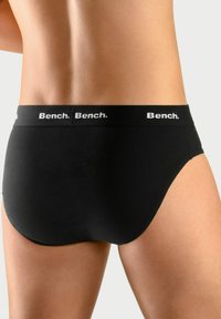 Schwarze Baumwollslips mit einem weichen Bund, der mehrfach mit dem weißen "Bench."-Logo bedruckt ist. Glatte Textur und enganliegendes Design.