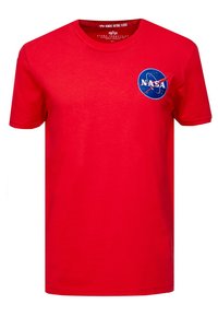 Červené tričko s krátkým rukávem s nášivkou loga NASA na levé hrudi a značkováním "Alpha Industries" uvnitř límce.