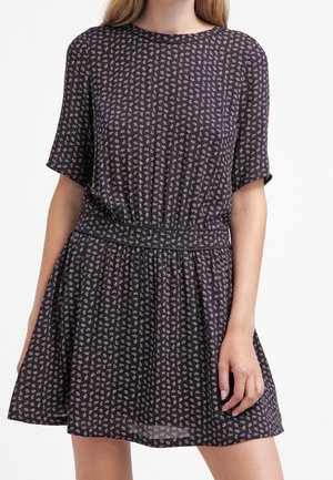 Femme portant une robe sombre à manches courtes avec un petit motif floral rose et une taille ajustée.