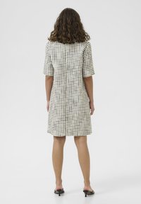 Provjeren haljina kratkih rukava u crnoj i bijeloj boji, s opuštenim krojem, koja pada iznad koljena, s ravnim šavom na leđima i bez vidljivih dijelova.