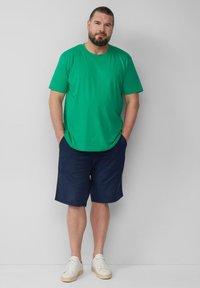 Zielona, krótko rękawowa koszulka, granatowe szorty i białe sneakersy. Koszulka ma okrągły dekolt, szorty mają kieszenie i teksturowany materiał.