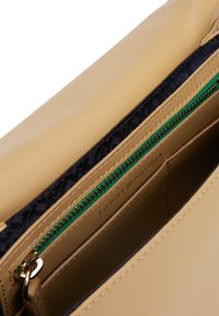 Interno di una borsa in pelle color tan, con una fodera a motivi navy, dotata di una cerniera verde e hardware dorato. Etichetta del marchio visibile all'interno.