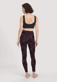 Zwarte sportbh met brede bandjes, gecombineerd met high-waisted legging in een donker maroon tie-dye patroon, gemaakt van gladde stof, enkel lengte.