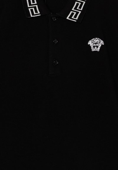 Camiseta polo negra con un patrón geométrico blanco en el cuello y un pequeño logo bordado en blanco de una cabeza en el pecho.