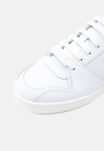 Κοντινό πλάνο του μπροστινού μέρους ενός λευκού δερμάτινου αθλητικού παπουτσιού με λευκά κορδόνια και λεπτές ραφές σε φωτεινό φόντο.