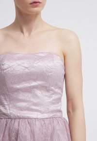 Ärmlös klänning i ljus lavendel med spetsöverdrag, satinliv och tylskjorta. Har ett texturerat spetsmönster och slät yta.