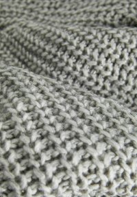 Gros plan d'un tissu tricoté gris clair montrant des boucles de fil tissées texturées et un motif de points doux et épais.