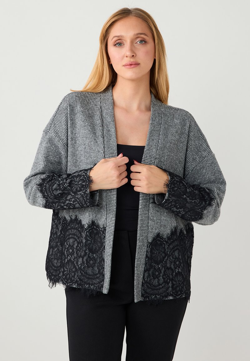 Cardigan gris côtelé avec bordure en dentelle noire aux manches et à l'ourlet. Ouvert sur le devant, coupe ample, tissu texturé.