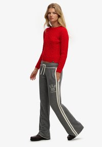 Rød kabelstrikket sweater med rund halsudskæring, kombineret med grå joggingbukser med hvide sidestriber og U.S.A. 83 logodetalje.