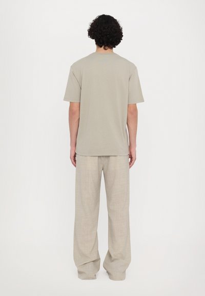 Lichtgrijs T-shirt met korte mouwen van zachte stof, gecombineerd met lichtbeige losvallende linnen broek, die een ontspannen silhouet laat zien.