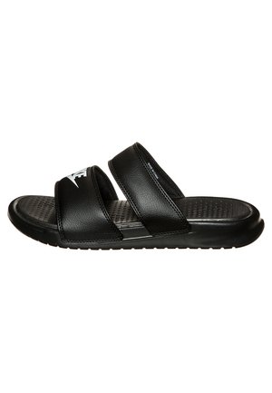 Sort slip-on sandal med to brede remme, tekstureret fodseng og en hvid logo på den øverste rem, vist mod en hvid baggrund.