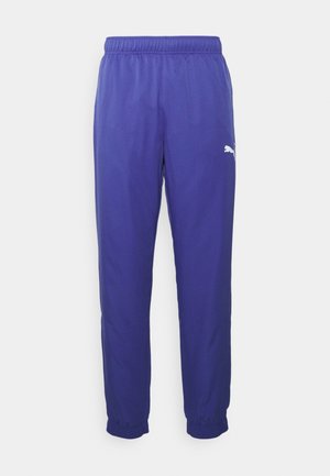 Fioletowe spodenki sportowe z elastycznym paskiem w talii, zwężanymi mankietami i białym logo na lewej nodze. Wykonane z lekkiego materiału.