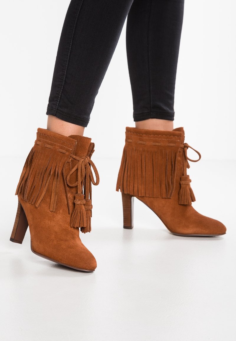 Brązowe zamszowe botki za kostkę z frędzlami, chwostami i spiczastym noskiem. Posiadają szpilkowy obcas oraz teksturowane boki.