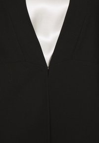 Blazer noir avec un col en V, fermeture éclair et une doublure en satin lisse. Le tissu a une texture nette.