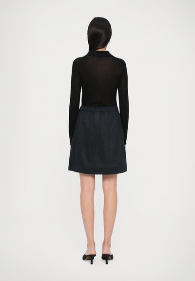 Svart långärmad topp som matchas med en mörk kjol. Outfiten har en figursydd kropp och en utsvängd nederdel, med subtil textur och en slät yta.